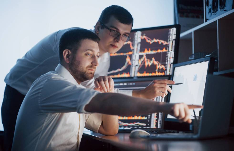 Team of stockbrokers are having a conversation in a dark office with display screens. Analyzing data, graphs and reports for investment purposes. Creative teamwork traders.